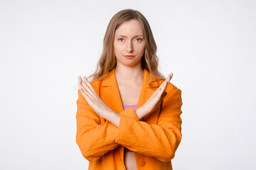 Please stop. Serious young woman insists on you quitting, rejecting, prohibit something, making cross gesture, standing over white background in orange blazer