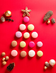 Christmas background with macaroons on red, french cakes in the shape of a Christmas tree with cones and Christmas balls. Vertical orientation, top view.