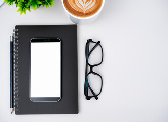 Top view of mock up modern workspace with blank screen smartphone, Coffee cup, Notebook, Pencil,...