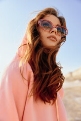 Stylish woman in pink hoodie and sunglasses standing confidently in the desert