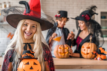 Fototapeta premium Portrait of smiling girl with pumpkin. Happy family preparing for Halloween. Woman and children wearing costumes celebrating posing with carved pumpkins looking at camera. Celebration concept