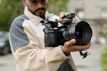 Man adjusting settings on a high-end camera during outdoor shoot, focusing on capturing the perfect shot Wearing casual attire and concentrating on the task