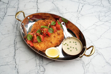 Fried sliced wiener schnitzel on a frying pan with herbs