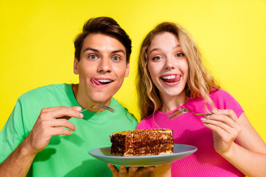 Photo of two nice young people eat large piece cake wear t-shirt isolated on bright yellow color background
