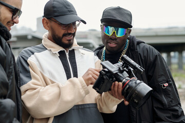 Group of filmmakers collaborating on film project, examining professional camera equipment and discussing scene by urban location enaged in creative process sharing ideas