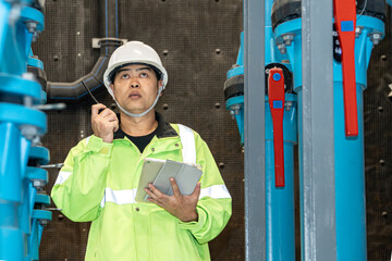 asian man worker in protective uniform and with hardhat using tablet for checking temperature in pipes Factory interior.