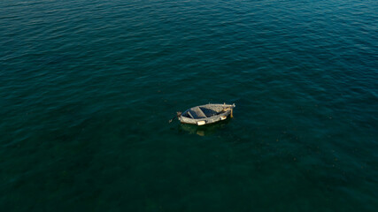Aerial view of a one small fishing boat anchored in the middle of the sea. The boat is empty and lonely.