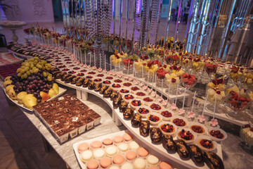 Luxury candy bar on golden wedding. Candy bar decorated by flowers standing of festive table with deserts, and cakes, strawberry tartlet, cupcakes and macarons. Wedding. Reception Tartlets. Catering