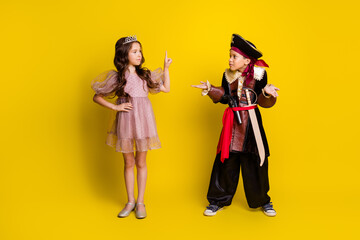 Full body portrait of two small kids point finger shrug shoulders halloween pirate princess costume isolated on yellow color background