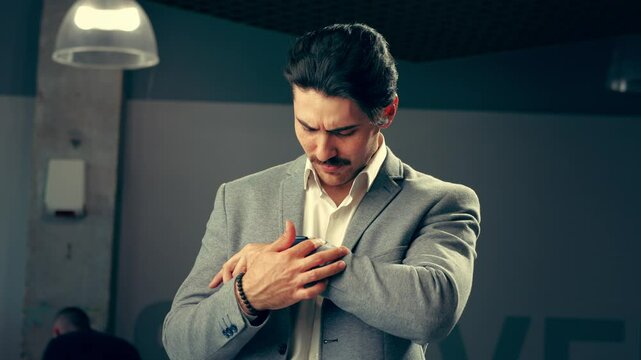 A man in a gray suit reflects thoughtfully while adjusting his cufflinks in an elegant urban setting