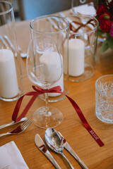 Elegant wedding table setting with a wine glass tied with a red ribbon, white candles, and stylish...