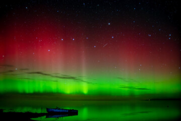 beautiful green red northern lights on the lake in autumn night with a lonely boat