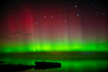 beautiful green red northern lights on the lake in autumn night with a lonely boat