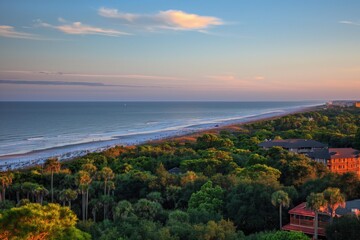 Obraz premium Serene beach scene at sunset with vibrant orange and pink sky. Palm trees on beach, ocean horizon in distance. Buildings silhouetted against sunset colors. Light brown sand, calm atmosphere.