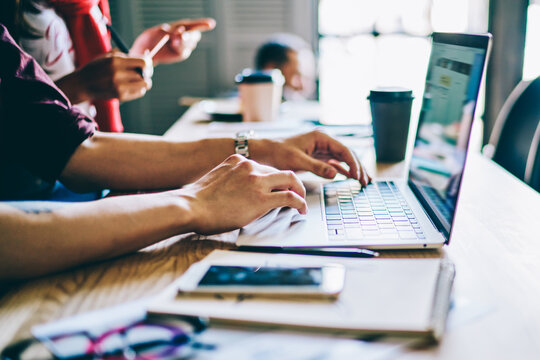 Cropped image of male hands typing text article via application on laptop computer using free internet connection during distance job in coworking space, courses for IT professionals at netbook