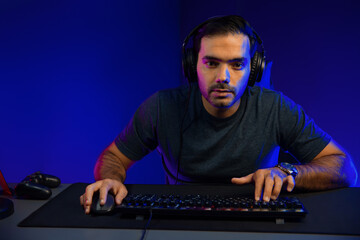 Smart gaming streamer concentrating gaming players trying to pass the level at mission completed, using headset and mic for communicate others on streaming live at neon lighting studio room. Surmise.