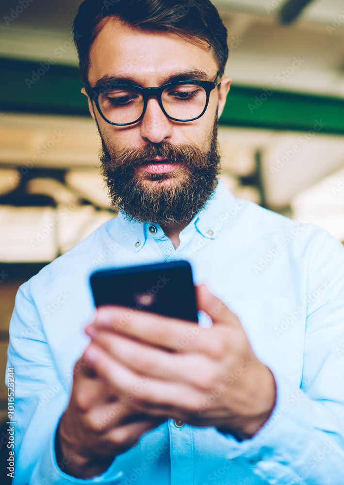 Poster bearded caucasian hipster guy sending sms message via multimedia application on mobile phone, young 