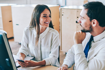 Obraz premium Cheerful male and female colleagues discussing video from social network during break near office desktop, successful professional man and woman in formal wear enjoying live communication indoors