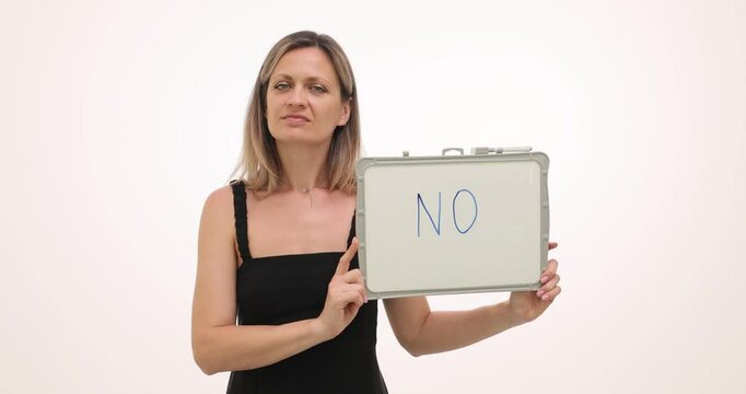 Woman shakes head and shows whiteboard with word NO on white background. Blonde in tank top with serious expression shows disagreement slow motion
