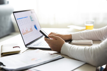 창가가 있는 거실에서 스마트폰과 노트북으로 작업하는 재택근무중인 여성 