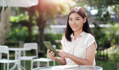 Asian business woman working outside freelancer using digital tablet device wireless remote communication technology, connectivity online worker casually enjoying outdoor in nature at cafe sunlight.