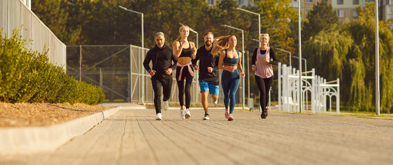 A group of athletic people are running along the street in the city. Men and women doing sports jogging. Runners at the local stadium, natural light. Leisure time for colleagues
