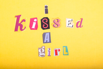 Phrase I Kissed a Girl spelled in cut out newspaper style typography, isolated on yellow background.