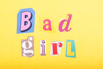 Phrase Bad Girl spelled in cut out newspaper style typography, isolated on yellow background.