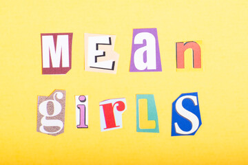 Phrase Mean Girls spelled in cut out newspaper style typography, isolated on yellow background.