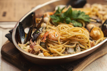 Hot plate of delicious spaghetti with mussel, clam, shrimps and squid on wooden cutting board.