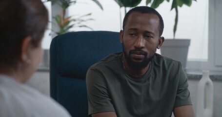 Depressed African American military man with PTSD talks, shares feelings during consultation with psychologist. Female psychotherapist provides therapy to war veteran. Post traumatic stress disorder.