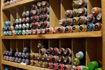 Long wooden shelves with stacks of unopened cans containing graffiti paints of various colors in modern art and craft shop