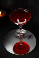 Vampire's Kiss Cocktail. Dracula's Blood Cocktail or Mocktail on dark background with reflection in mirror. Drink for Halloween with plastic vampire teeth as a garnish. Festive food and beverages.