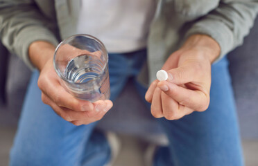 Sick man taking his daily dose of medicine at home. Closeup hands of an adult man holding one...