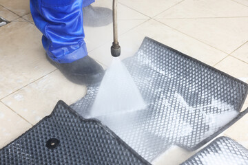 Man washing rubber car mats with high pressure water jet indoors, closeup