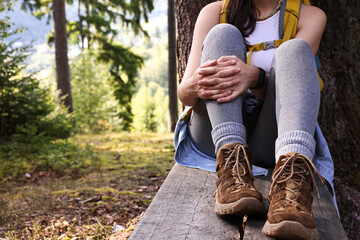 Young hiker sitting on wooden bench in forest, closeup