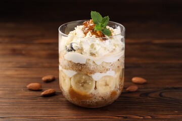 Tasty trifle dessert. Sponge cake, banana and whipped cream in glass on wooden table, closeup