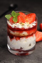 Tasty trifle dessert. Strawberries, sponge cake and whipped cream in glass on grey table