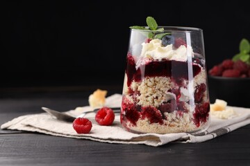 Tasty trifle dessert. Berries, sponge cake and whipped cream in glass on black wooden table, space for text