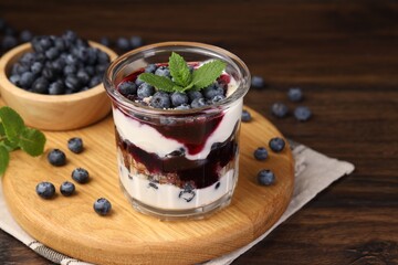 Tasty trifle dessert. Blueberries, sponge cake and whipped cream in glass on wooden table