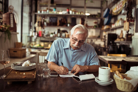 Senior bistro owner writing notes after busy day