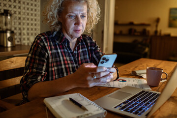 Worried elderly woman looking at laptop while managing finances at night