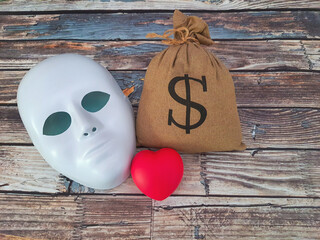 Bag of money, heart and mask on an old wooden table.