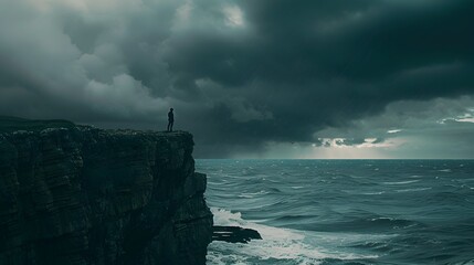 Lone figure standing on cliff overlooking stormy ocean horizon