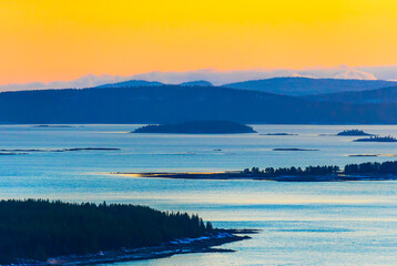 Stunning sunset view over tranquil waters of the White Sea and islands. The golden hues of the setting sun illuminate the calm waters. A picturesque landscape of islands and distant mountains