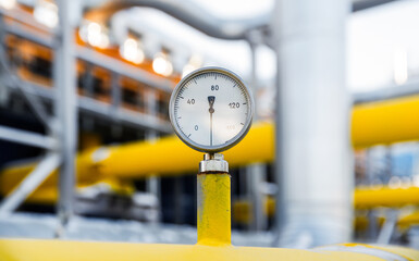 A pressure gauge measures the pressure of gas flowing through a bright yellow pipeline in a busy...