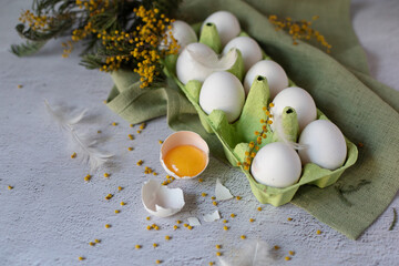 a dozen chicken eggs on a light background with a broken yolk