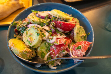 Vibrant georgian salad of fresh tomatoes, cucumbers and onions, seasoned with herbs and a light sauce of nuts, served in a blue bowl