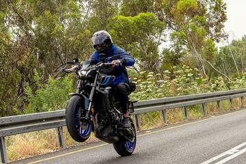 A motorcycle racer performs a difficult and dangerous stunt on his motorcycle. Riding on the back...
