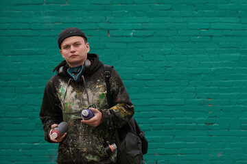 Naklejka premium Guy in stylish casualwear looking at camera while holding two unopened cans with graffiti paints before creating artwork on wall
